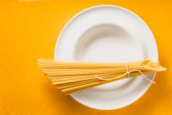 Sekumpulan spageti mentah di piring putih pada tampilan atas latar belakang kuning — Stok Foto