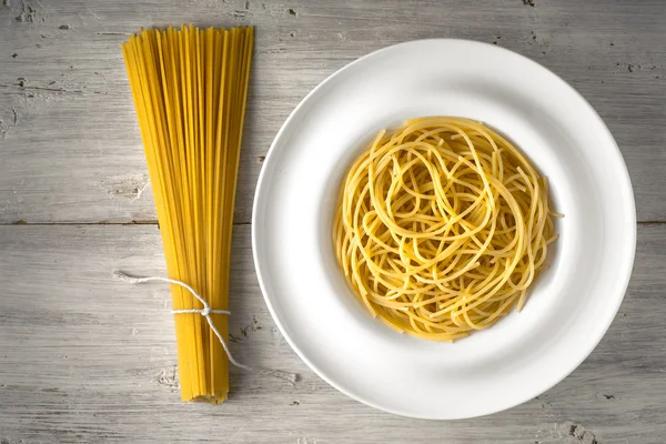 Raw and cooked spaghetti on the white wooden table top view — Stock Photo, Image