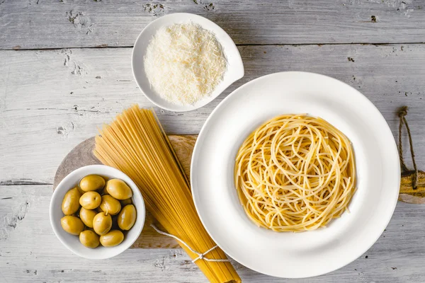 Esparguete cru e cozido com azeitonas e queijo na vista superior da mesa de madeira branca. Conceito de cozinha italiana — Fotografia de Stock