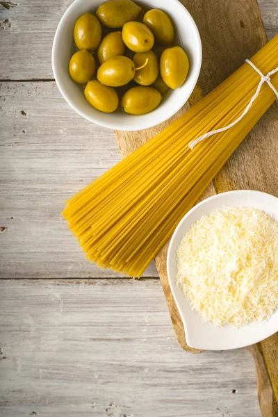 Espaguete cru com azeitonas e queijo na mesa de madeira branca vertical — Fotografia de Stock
