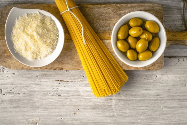 Espaguete cru com azeitonas e queijo na vista superior da mesa de madeira branca — Fotografia de Stock