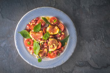 Taş masaüstü görünümünde seramik tabak üzerinde incir ve kiraz domates ile meyve salatası