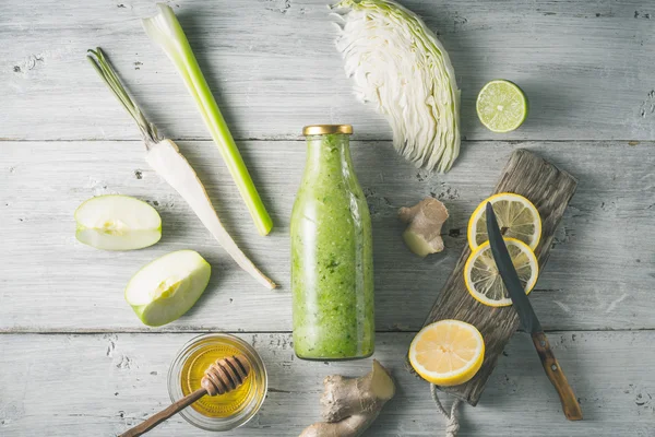 Glazen fles met groente smoothie met verschillende ingrediënten op het witte houten tafelblad uitzicht — Stockfoto