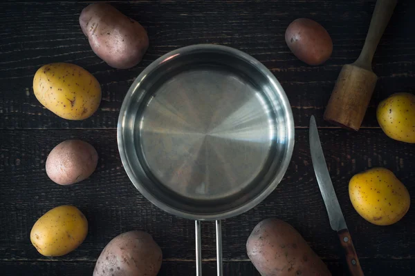 Kochtopf umgeben von rohen Kartoffeln auf dem hölzernen Tisch — Stockfoto