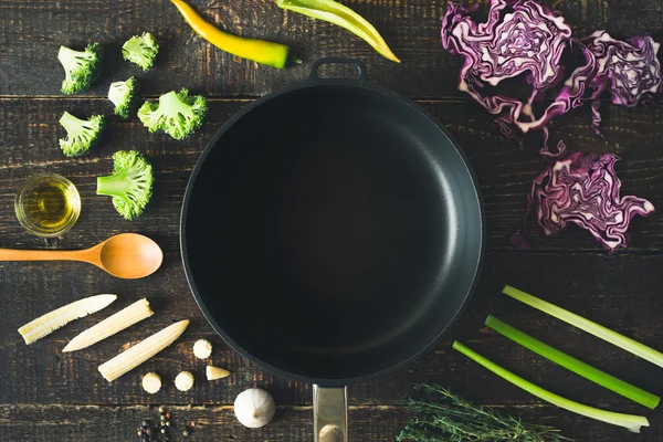 Empty pan surrounded by vegetable and seasoning on the wooden table top view — Stock Photo, Image