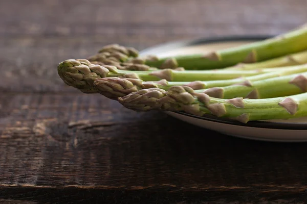 Asperges op een witte plaat op de houten tafel — Stockfoto