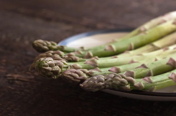 Asperges op een witte plaat op de houten tafel — Stockfoto