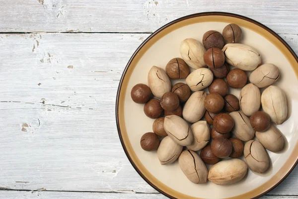 Pecan e macadâmia na placa no fundo branco — Fotografia de Stock