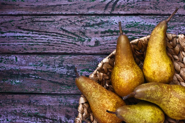 Pears in a braided bowl on a purple background — Stock Photo, Image