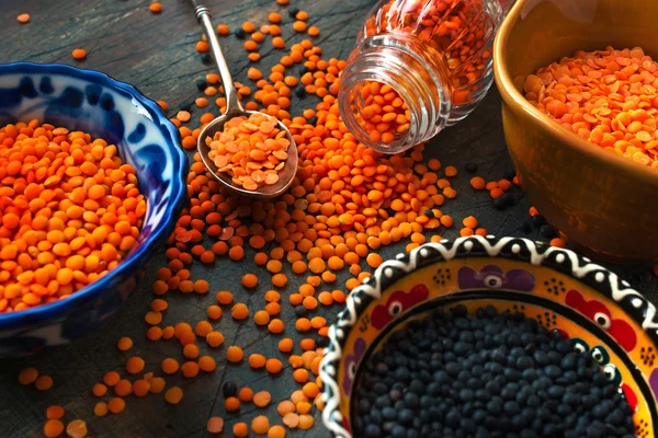 Schwarze und rote Linsen in den Keramikschalen auf dem dunklen Hintergrund — Stockfoto