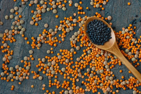 Rote und schwarze Linsen und ein Kochlöffel auf dem Holzgrund — Stockfoto