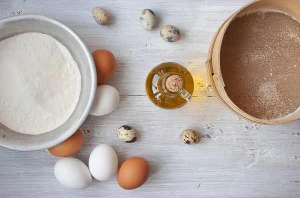 Eggs, flour and a bottle of olive oil on the white wooden table — Stock Photo, Image