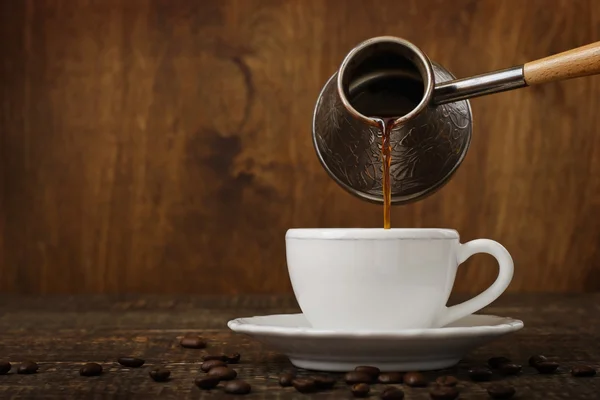 Dark coffee pours from a copper jezve into a white cup — Stock Photo, Image