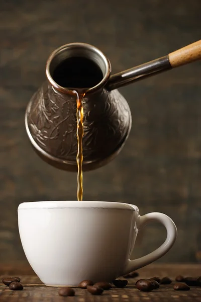 Dark coffee pours from a copper jezve into a white cup — Stock Photo, Image