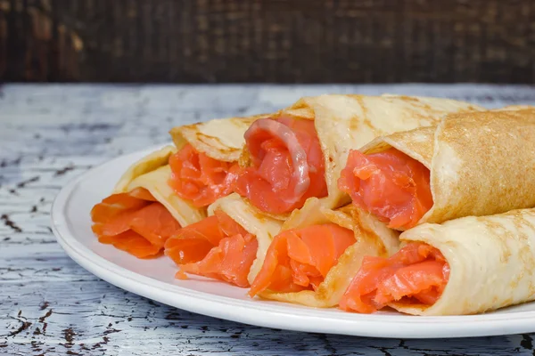 Rolls from pancakes with salmon on the white ceramic plate — Stock Photo, Image