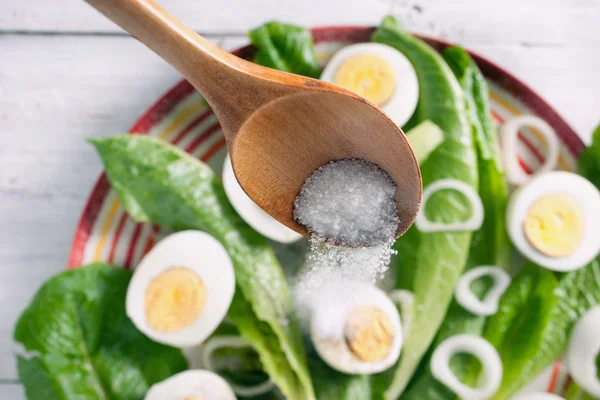 La sal vierte de la cuchara de madera en una ensalada — Foto de Stock