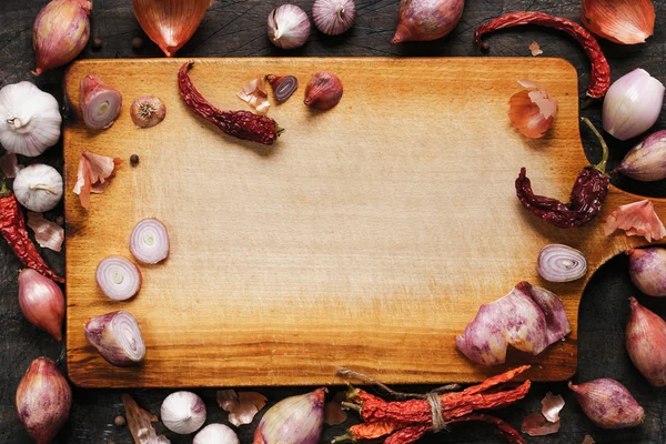 Dřevěná deska s cibuli, česnek a pepř pozadí — Stock fotografie