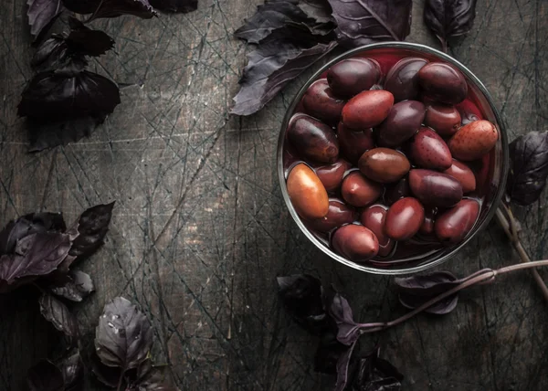 Kalamata zeytin eski koyu ahşap masa üzerinde kırmızı fesleğen ile cam tabak üzerinde salamura