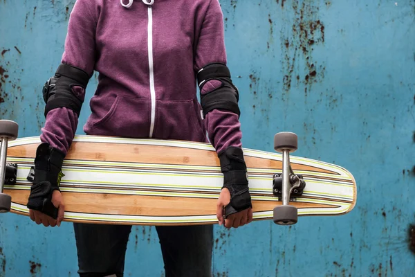 Longboard in de handen tegen de oude blauwe muur — Stockfoto