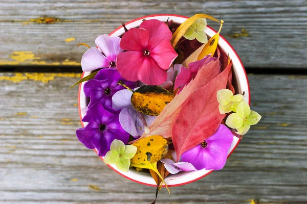 Hojas coloridas y flores en el cuenco de cerámica en la vieja mesa de madera —  Fotos de Stock