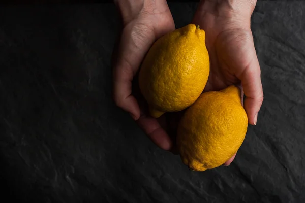 Dos limones en las manos sobre la mesa de piedra negra —  Fotos de Stock