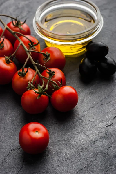 Rama de tomates con aceitunas y aceite de oliva en la mesa de piedra oscura —  Fotos de Stock
