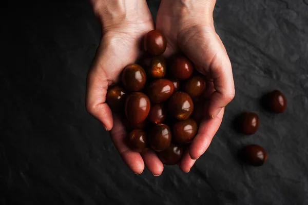 Eine Handvoll Tomaten in den Händen auf dem schwarzen Steintisch — Stockfoto