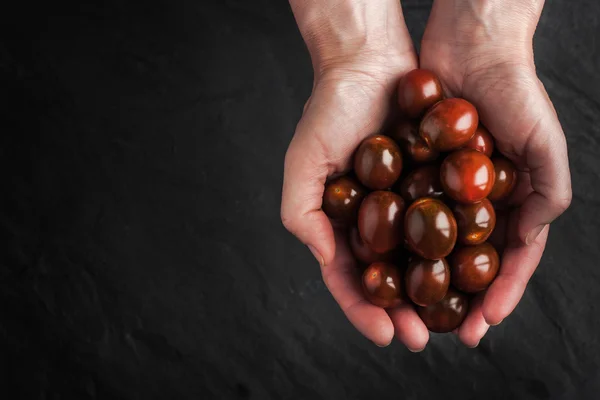 Tomates cereja nas mãos sobre a mesa de pedra preta — Fotografia de Stock