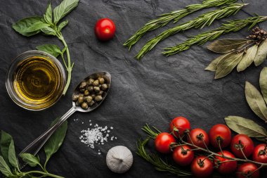 Herbs mix with tomatoes and olive oil on the black stone table