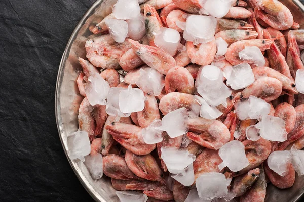 Frozen shrimps in the metal plate on the black stone table — Stock Photo, Image