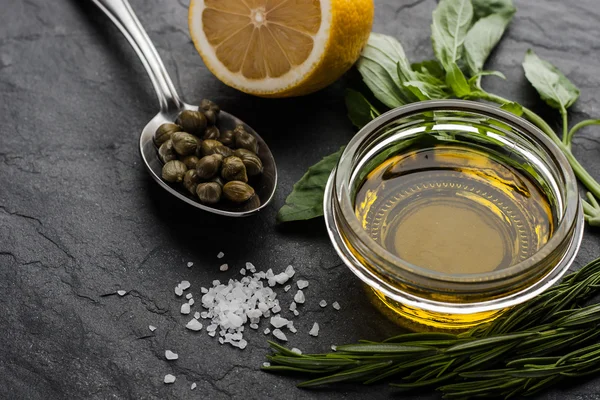 Olive oil on the glass bowl with lemon , capers and different greens — Stock Fotó