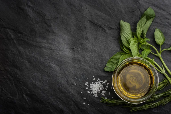 Olive oil  with different greens on the right side of the black stone table — Stockfoto