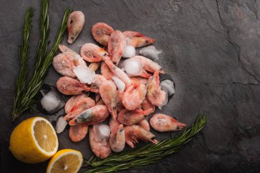 Frozen shrimps  with lemon and rosemary on the black stone table