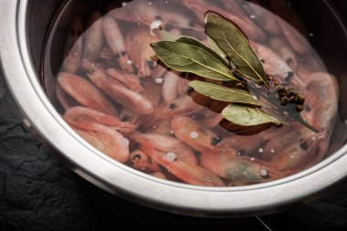 Fresh shrimps and bay leaf in the metal pot on the black stone table clipart