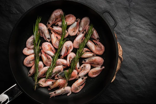 Prawns with sprigs of rosemary in the pan on the black stone table — Stock Photo, Image