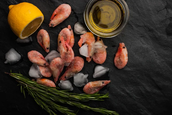 Camarões congelados com alecrim, limão e azeite sobre a mesa de pedra preta horizontal — Fotografia de Stock
