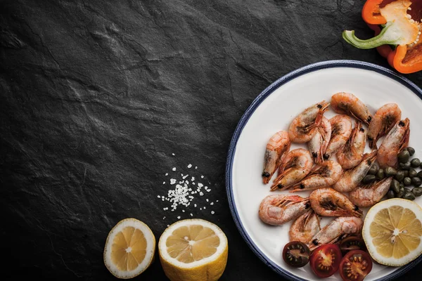 Grilled shrimps with lemon and vegetables on the ceramic plate on the black stone table — Stock Photo, Image
