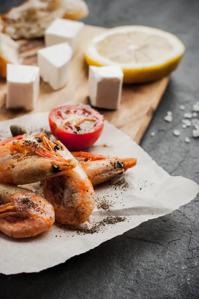 Grilled prawns on the peace of paper with tomatoes and cheese on the wooden board — Stock Photo, Image