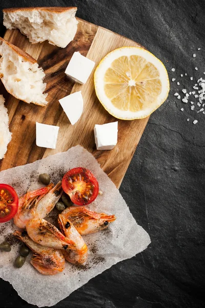 Grilled shrimps on the peace of paper with different snack on the black stone table vertical — Stock Photo, Image
