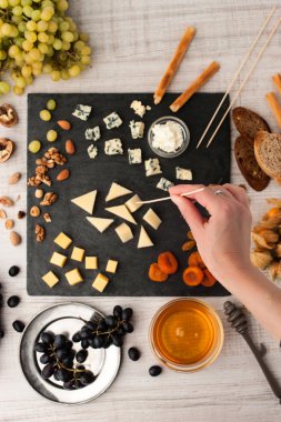 Assorted with cheese , fruits and nuts on the black stone with woman hand