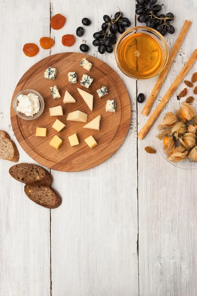 Frutas e queijos sortidos na mesa de madeira branca vertical — Fotografia de Stock
