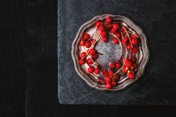 Красные ягоды веточка в винтажной металлической пластине на черном камне — стоковое фото