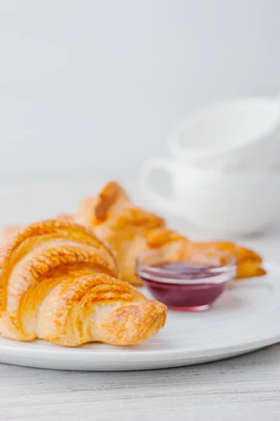 Croissant con marmellata di frutti di bosco e due tazze bianche sfocate — Foto Stock