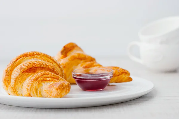 Croissant con confettura di frutti di bosco e due tazze bianche sfocate orizzontali — Foto Stock