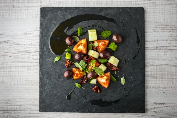 Vegetable salad with dried tomatoes and olives on the black stone top view — Stock fotografie