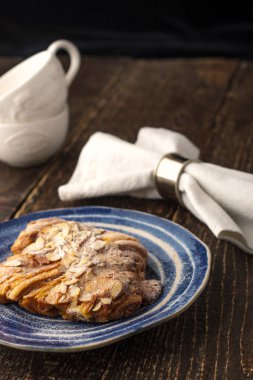 Croiisant with almond on the ceramic plate with two blurred cups and napkin