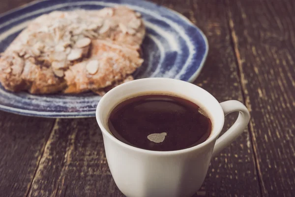 Taza de café con croissant desenfocado con almendra en el plato de cerámica azul — Foto de Stock