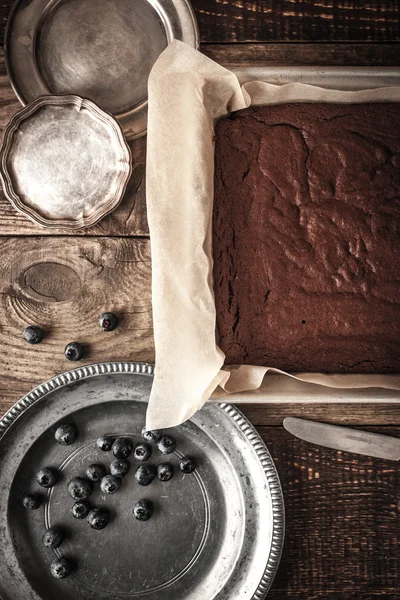 Schokoladenbrownie auf dem Backblech mit Blaubeere und Tellern senkrecht — Stockfoto