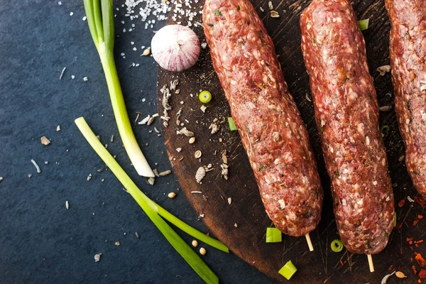 Raw kebabs with seasoning , onion and garlic on the wooden board — Stock Photo, Image