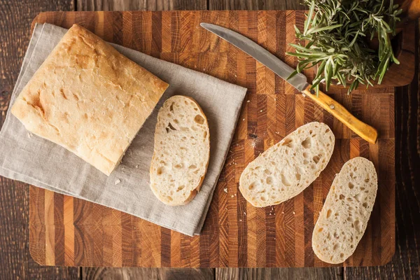 Нарезанный хлеб на деревянной доске с розмарином вид сверху — стоковое фото